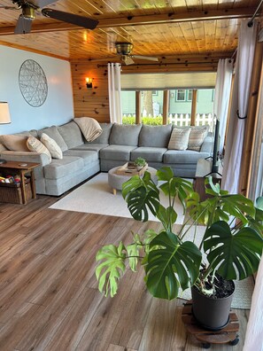 A cozy living room with a sectional sofa, wooden flooring, a ceiling fan, and a large potted plant.