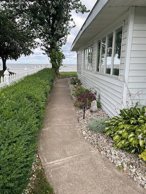 A pathway leading to a building with a white exterior, a white fence, and a view of the water.