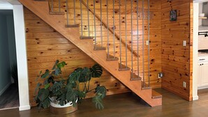 Un escalier en bois avec des rampes en métal, une plante en pot et, au fond, un coin cuisine.