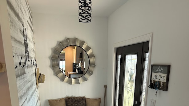 Un couloir avec un tapis gris, un banc muni de paniers, un miroir décoratif et une porte sur laquelle est apposée une plaque indiquant « Maison au bord du lac ».