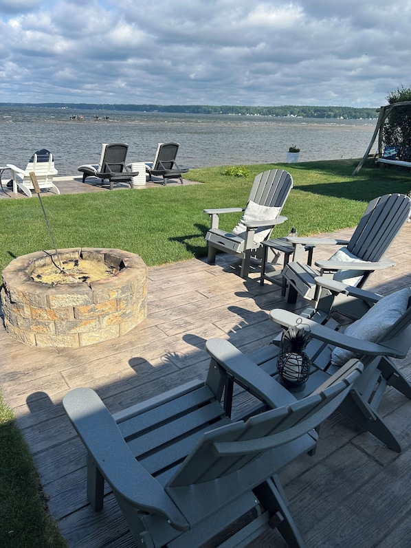 A deck with Adirondack chairs, a fire pit, and a view of the lake.