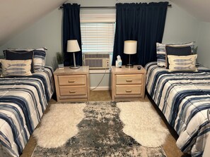 A bedroom with two beds, a desk, and a window with curtains.