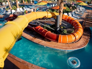 A water park with a large yellow slide, a circular water feature, and lounge chairs around a pool.