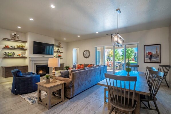 A modern living room with a fireplace, a sofa, a dining table with chairs, and a TV mounted on the wall.