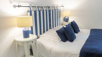 A bedroom with a bed, bedside table, lamp, and a wall-mounted air conditioner.