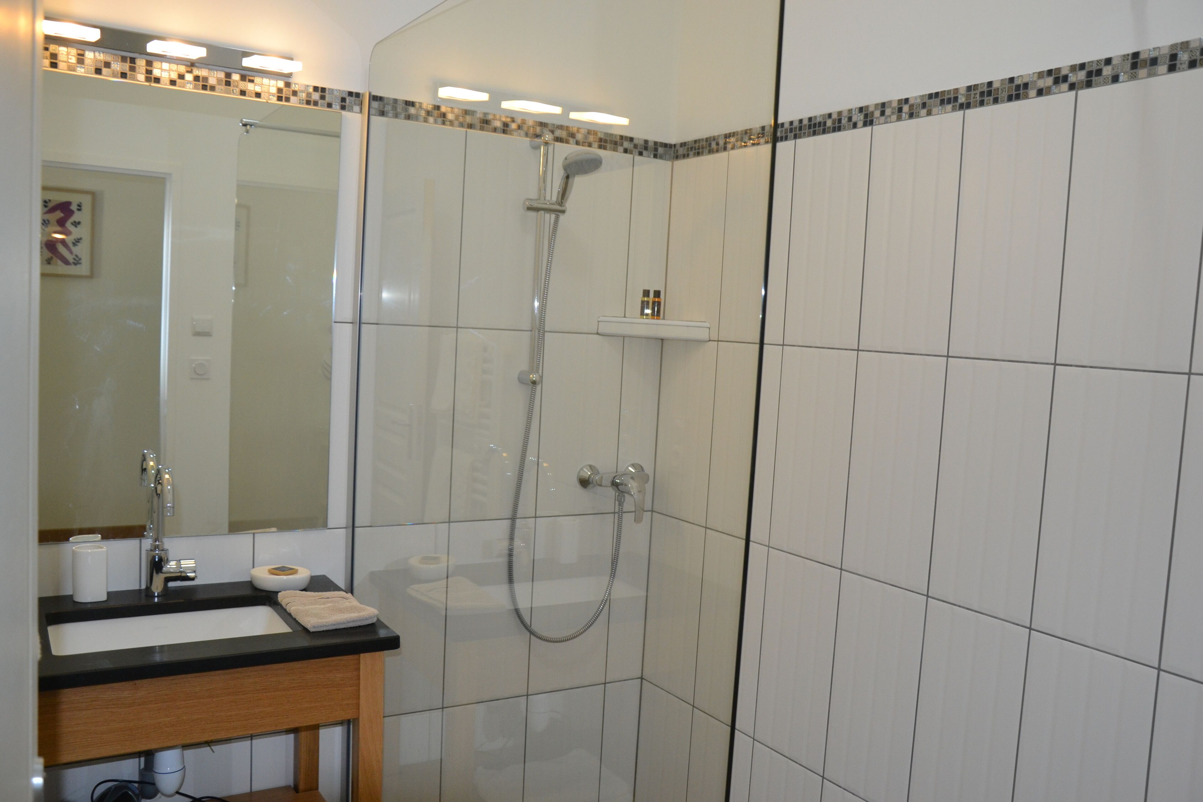 Ein Badezimmer mit einer Duschkabine, einem Waschbecken mit Spiegel und einem Ablagebereich für Pflegeprodukte.