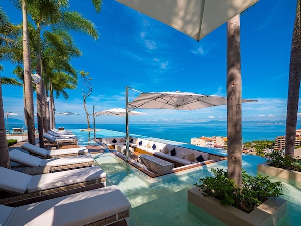 A poolside area with lounge chairs and umbrellas, overlooking a body of water.