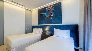 Camera d'albergo con due letti, un comodino con una lampada e un grande quadro appeso al muro.