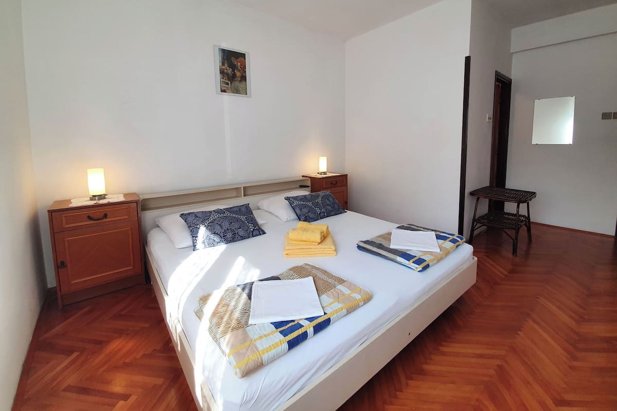 Una camera d'albergo con un letto grande, due comodini con lampade, un tavolino e uno specchio appeso al muro.