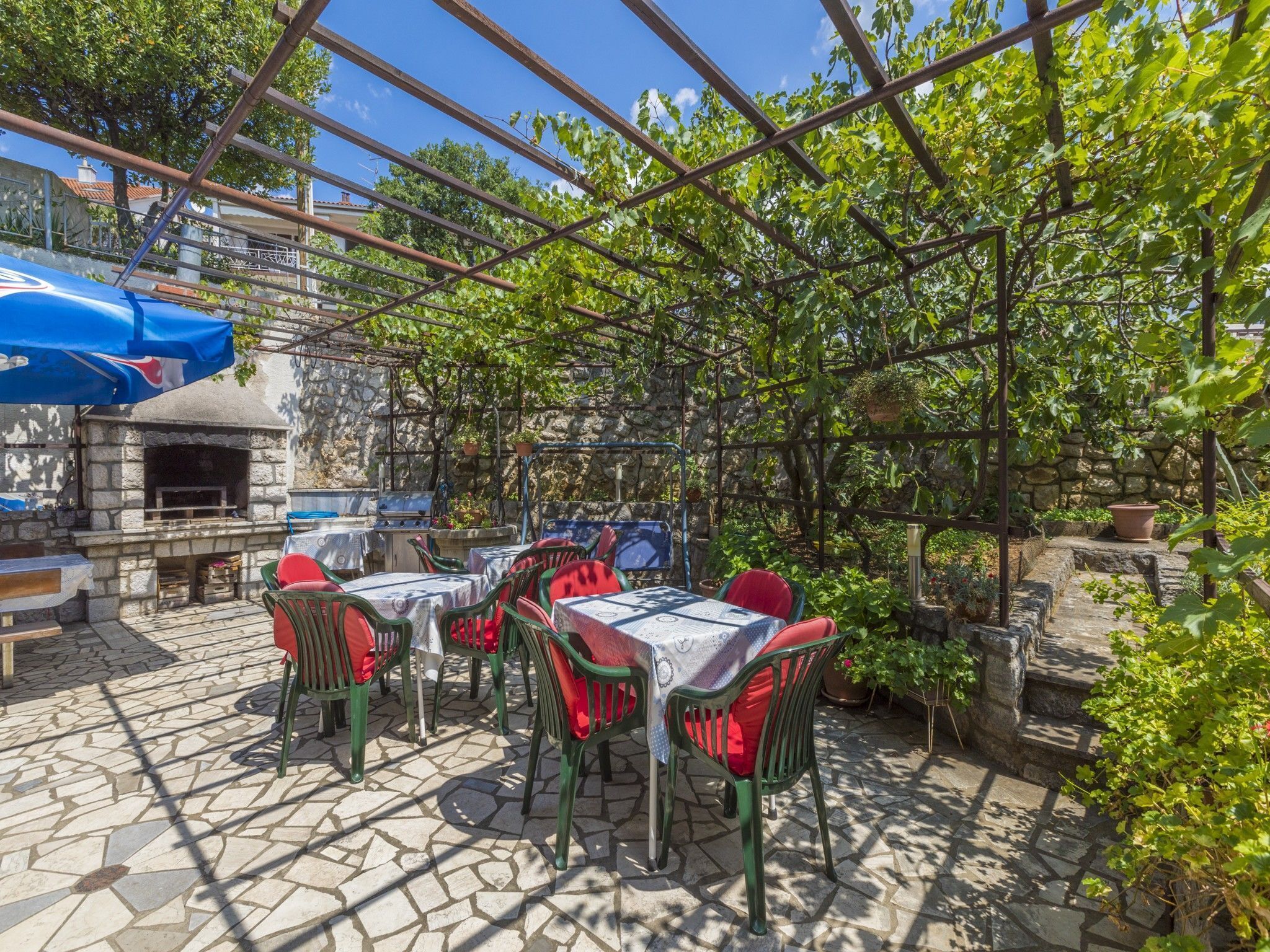 An outdoor patio with stone flooring, green metal chairs, and tables covered with white tablecloths.