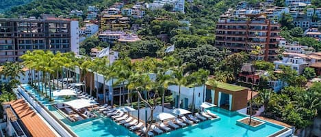 Una piscina sul tetto con sedie a sdraio e palme, circondata da edifici e uno sfondo montuoso.