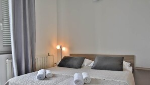 A neatly made bed with rolled towels, a bedside lamp, and a radiator. - Apartments Ruzica (Banjol)