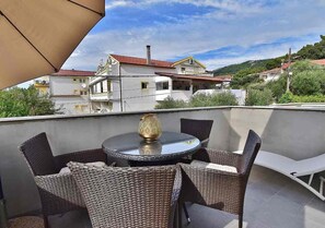 A balcony with wicker furniture and a table, overlooking a residential area with houses and greenery.