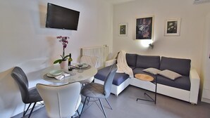 A modern living room with a dining area, a sofa, a TV mounted on the wall, and artwork on the walls. - Apartments Ruzica (Banjol)