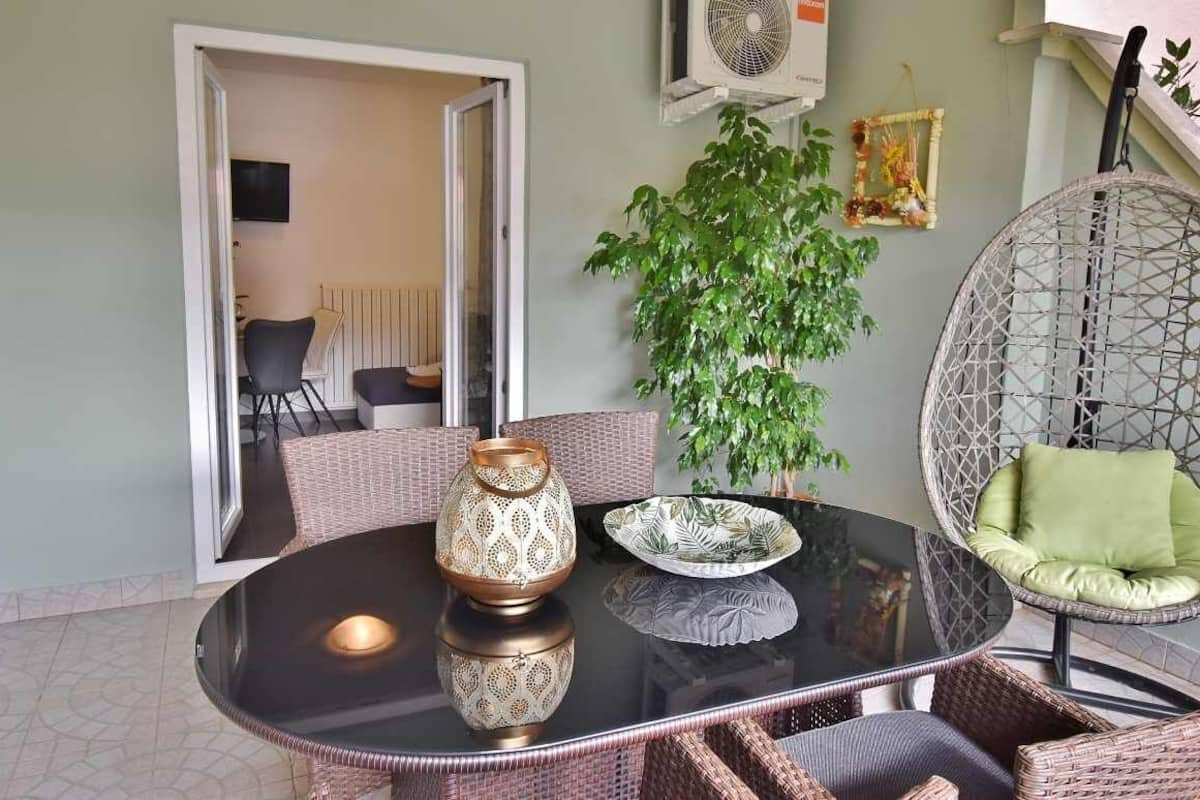 A round glass table with wicker chairs, a decorative vase, and a potted plant.