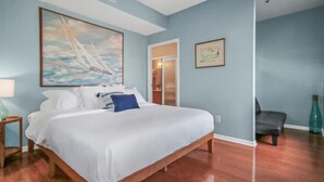 Un dormitorio con una cama grande, una mesita de noche, una silla y una puerta que da a otra habitación.