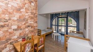 A room with a stone wall, a wooden table with chairs, a bed, and a large window with curtains. - House Paklenica Stone ll (Seline)