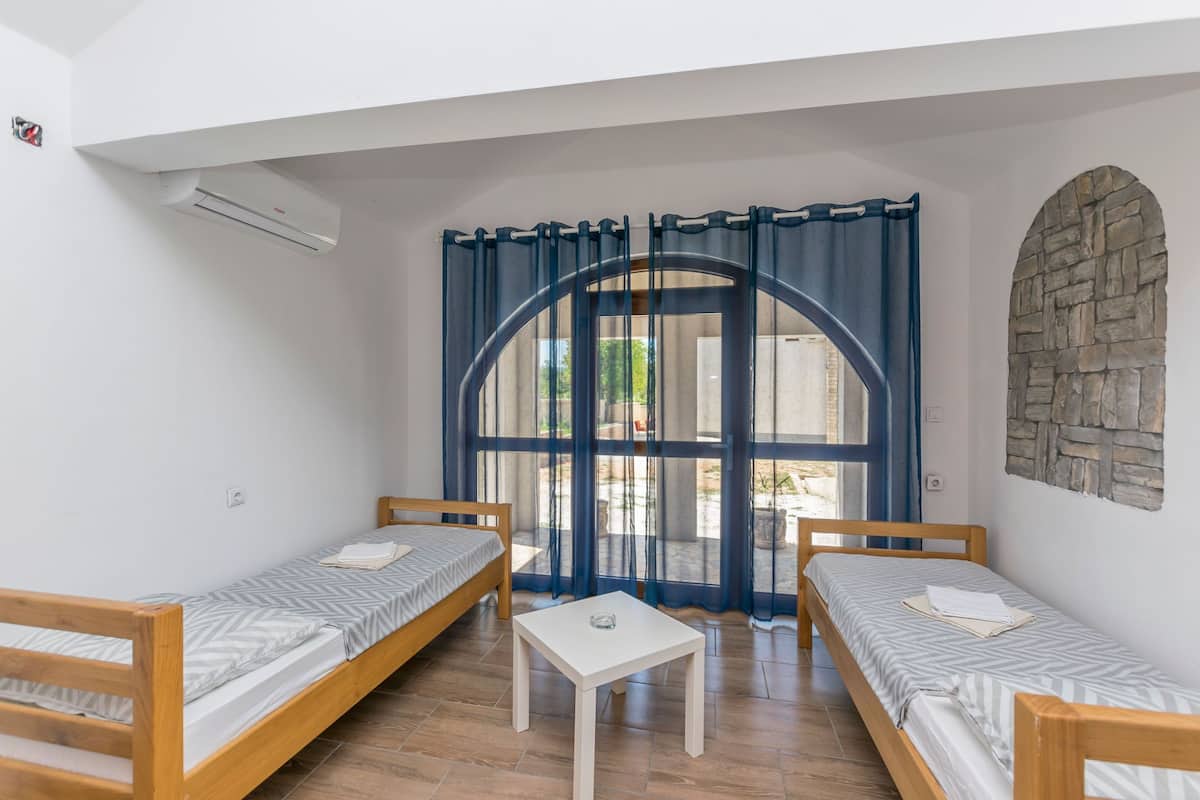 A room with two single beds, a small table, and a large window with curtains.