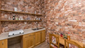 A compact kitchen with stone walls, wooden cabinets, and a dining area with a table and chairs. - House Paklenica Stone ll (Seline)