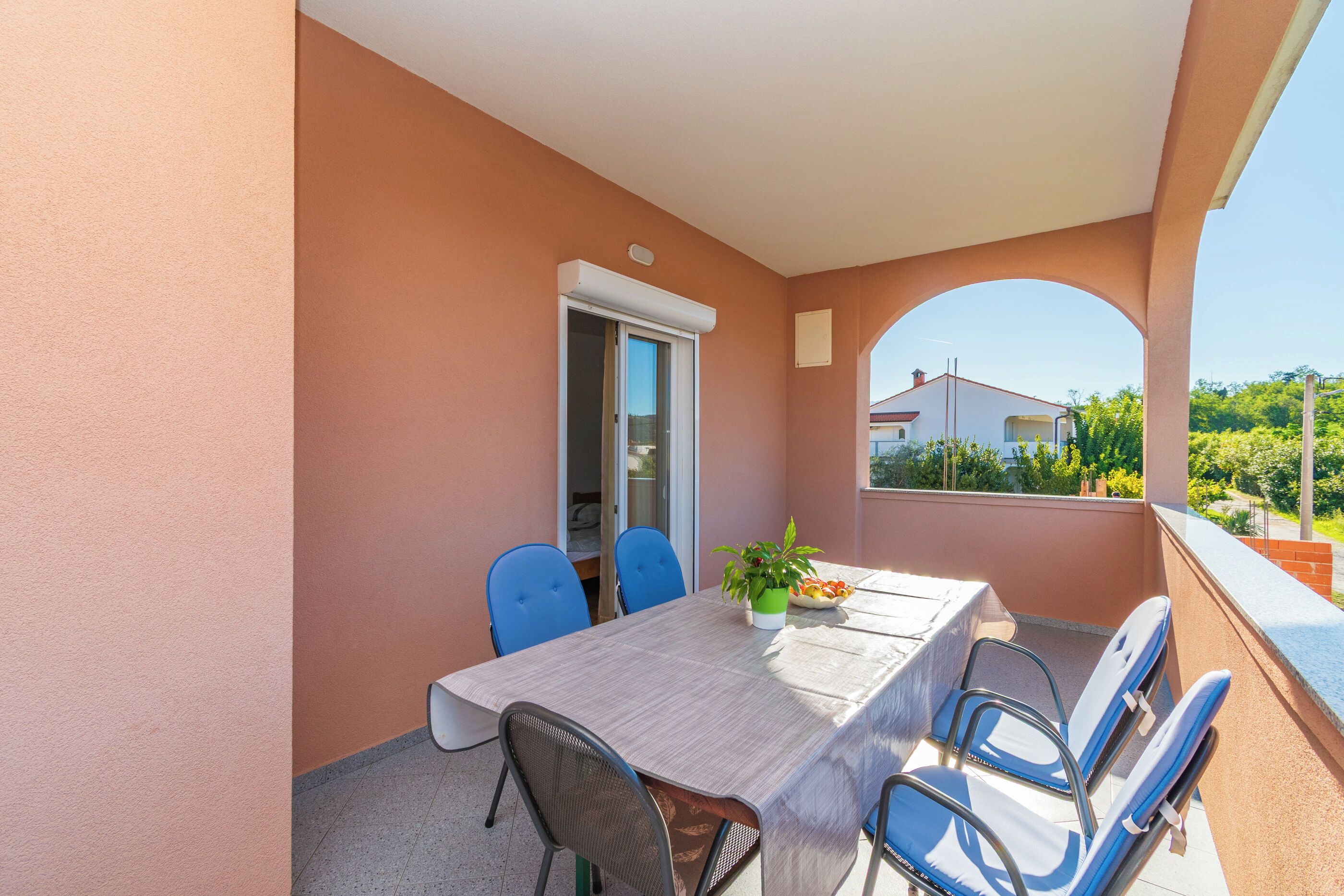 A balcony with a table and chairs, a potted plant, and a view of a building in the background.