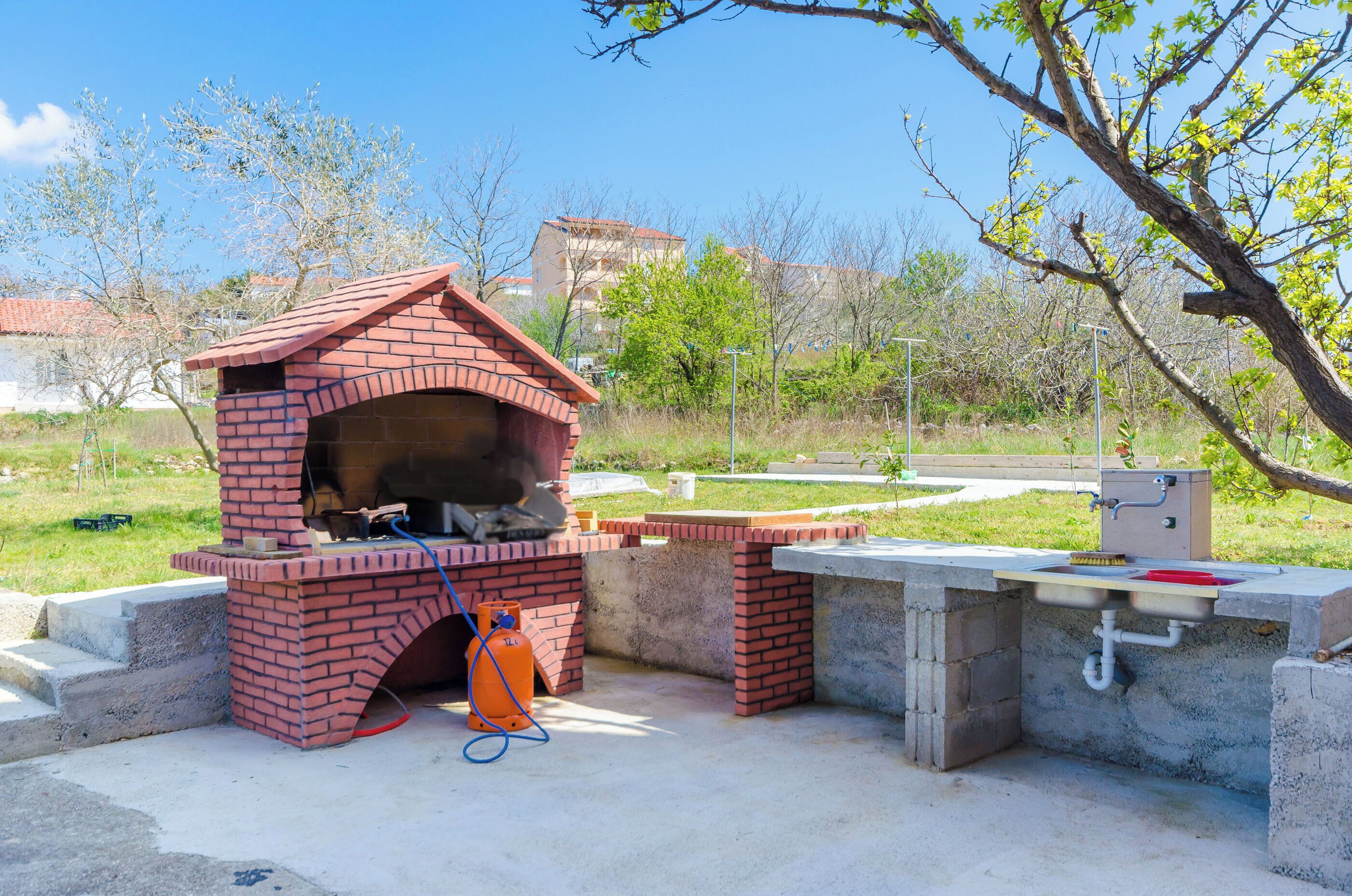 A brick outdoor kitchen with a chimney, a gas tank, and a concrete sink area.