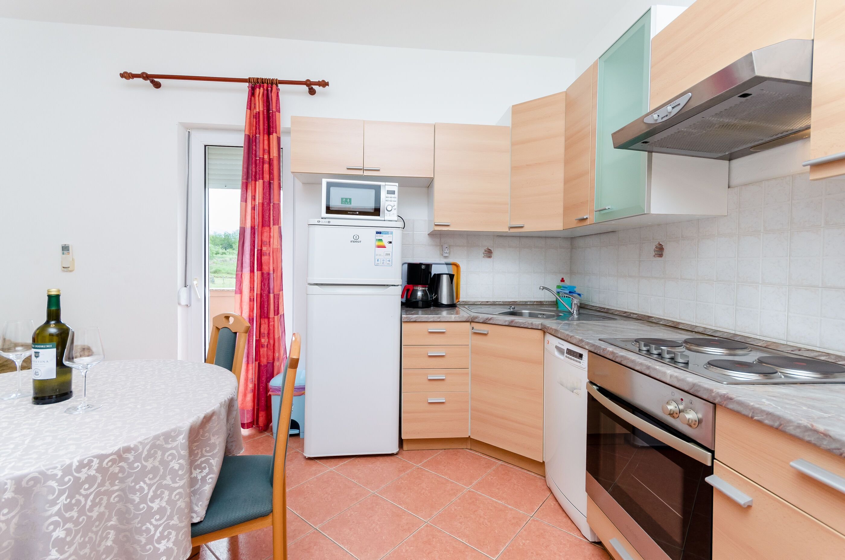 Cocina compacta con microondas, estufa y lavamanos. Hay una mesa de comedor con una botella y vasos.
