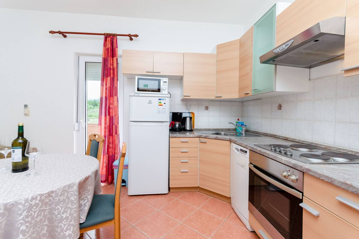 Cocina compacta con microondas, estufa y lavamanos. Hay una mesa de comedor con una botella y vasos.