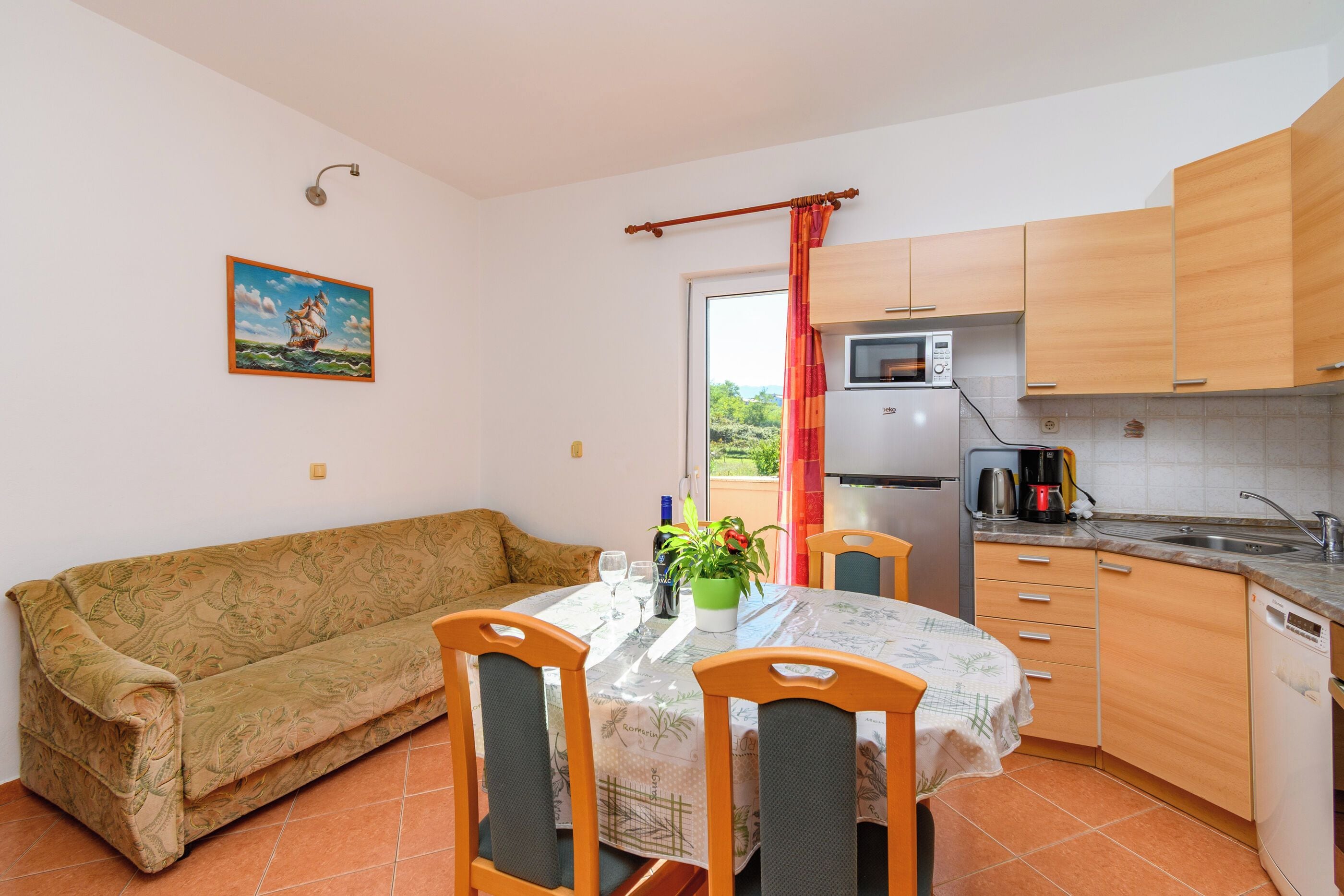 Cocina compacta con armarios de madera, una mesa de comedor con sillas, un sofá y un cuadro en la pared.