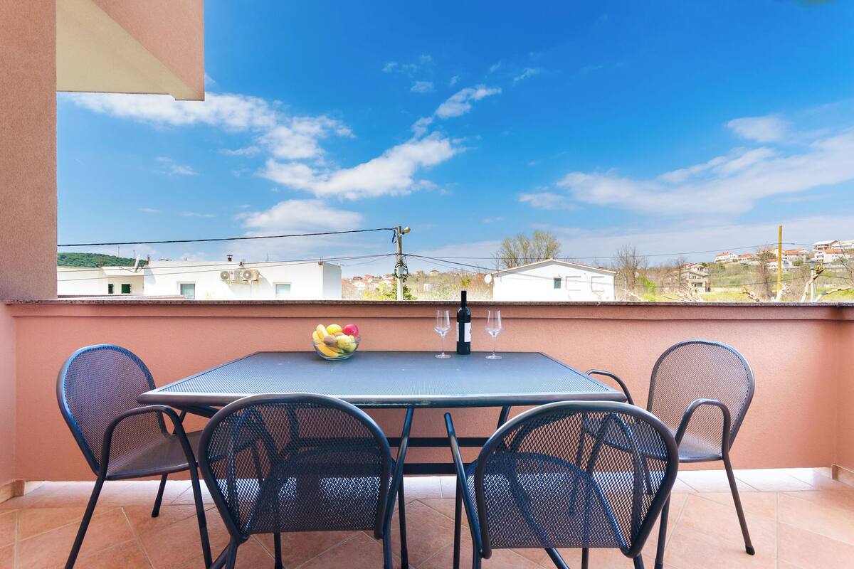 Un balcone con tavolo e sedie, una ciotola di frutta e una bottiglia di vino.