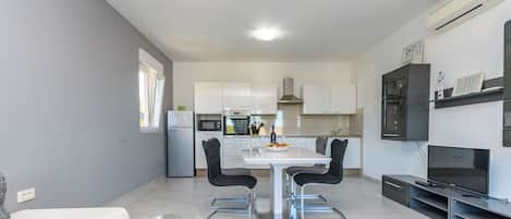 Una cocina moderna con armarios blancos, una mesa de comedor con sillas, un horno empotrado y un microondas.