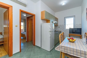 A compact kitchen with a refrigerator, a dining table with chairs, and a television.