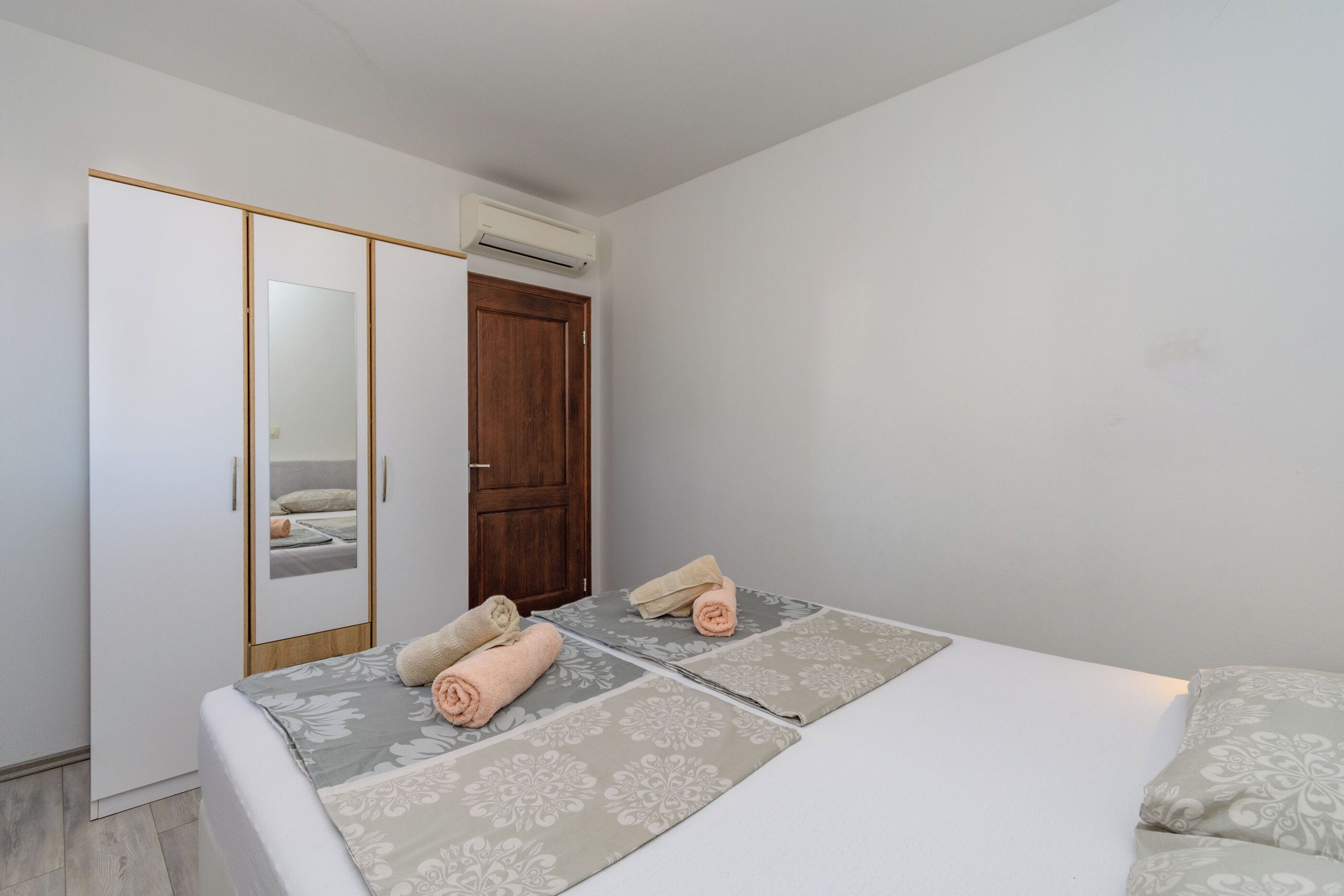 Une chambre avec un lit, deux serviettes enroulées, une armoire et un appareil de climatisation.