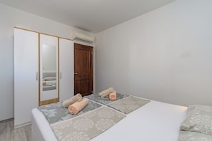 A bedroom with a bed, two rolled towels, a wardrobe, and an air conditioning unit. - Apartments and Room Ljubica (Lopar)