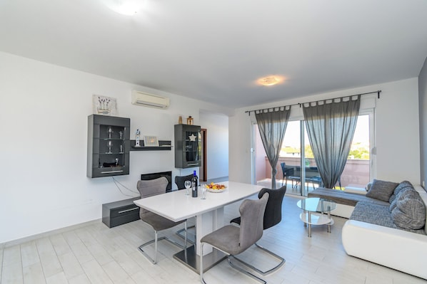 A modern living space with a dining table, chairs, a sofa, and a glass-top coffee table.