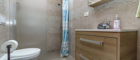 A bathroom with a toilet, a shower with a curtain, a sink with a soap dispenser, and a wooden cabinet.