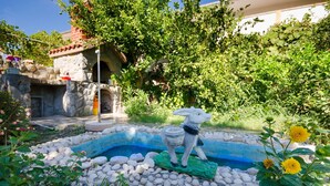 A garden with a decorative rabbit statue, a small pond, and surrounding greenery. - Apartments Elvira (Lopar)