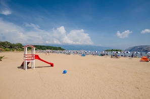 A beach with a lifeguard stand, umbrellas, and a tent.