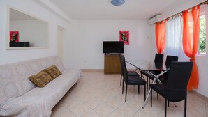 A living room with a sofa, TV, and dining area with chairs and a table. - Apartments Elvira (Lopar)