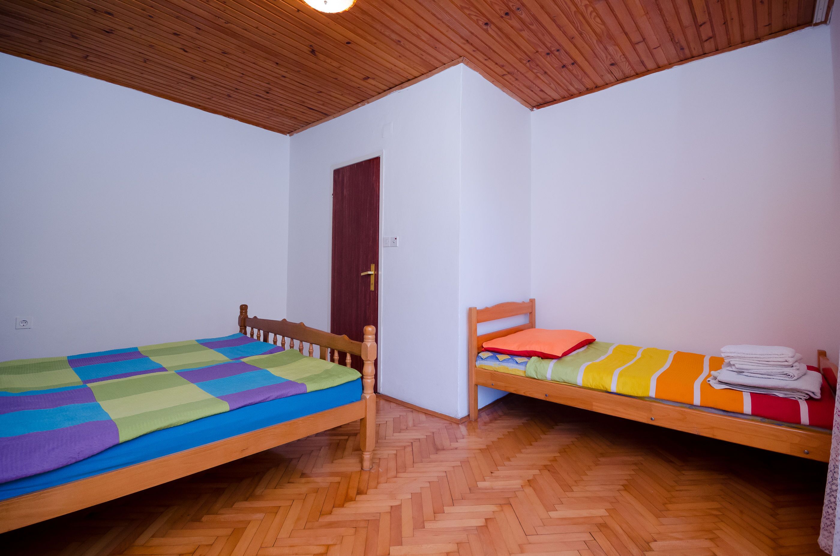 A room with two wooden beds, a wooden ceiling, and a herringbone floor pattern.