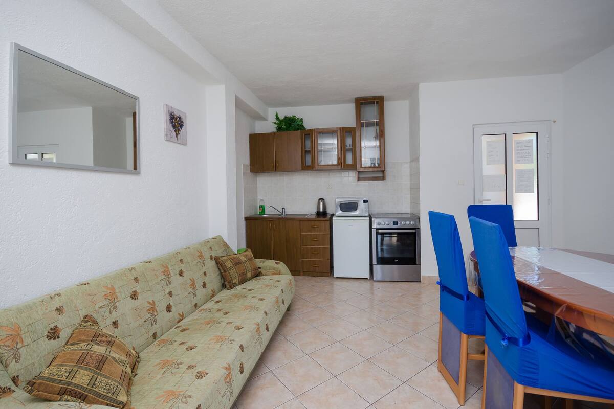 A compact living space with a sofa, a dining table with chairs, a kitchenette with cabinets, and a refrigerator.