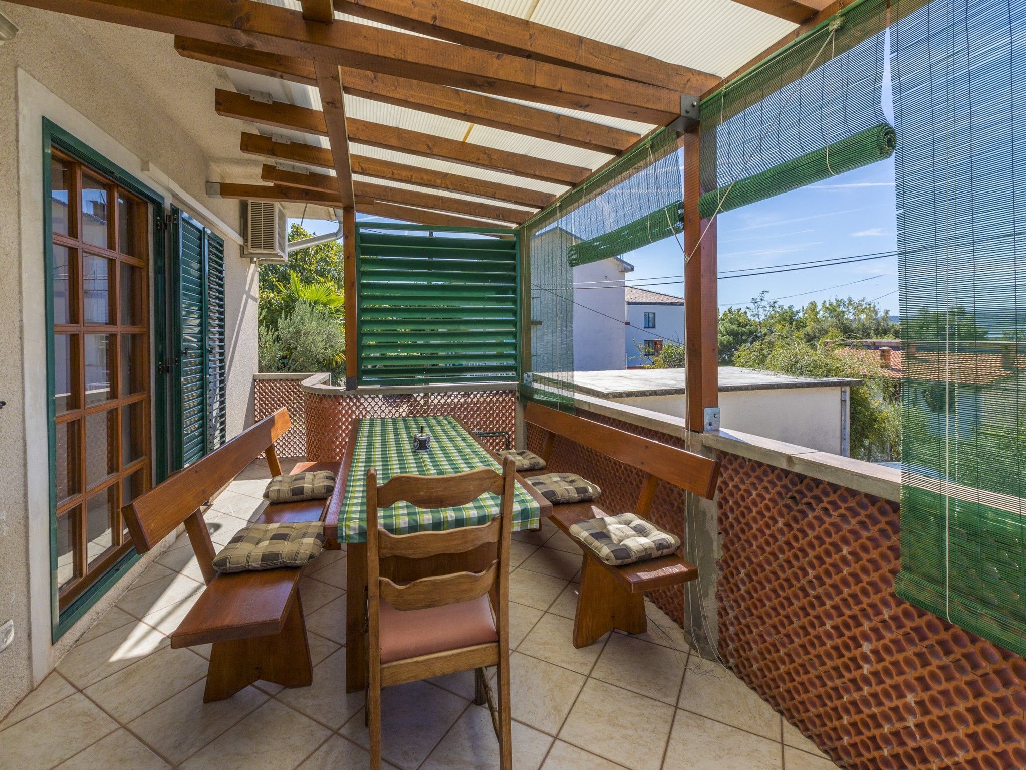 A covered patio with a table and benches, a view of the neighborhood, and a green mesh screen.
