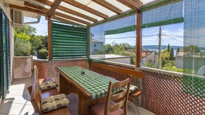 A covered patio with a wooden table and chairs, a view of the surrounding area, and a patterned wall. - House Haus Vlady (Crikvenica)