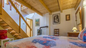 Un dormitorio con una escalera de madera, una cama con colcha colorida, un calentador y una silla.