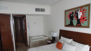 Una habitación de hotel con cama, mesita de noche, un cuadro y un baño visible a través de una puerta abierta.
