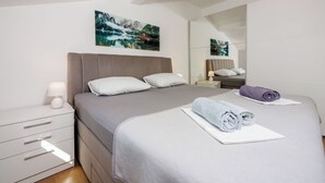 A neatly arranged bedroom with a bed, a bedside table with a lamp, a mirror, and a painting on the wall. - Apartment Davor (Dramalj)