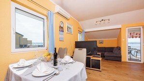 A dining area with a table set for four, a sofa, and a TV in the background. - Apartment Davor (Dramalj)