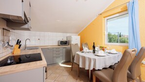 A modern kitchen with a dining area, featuring a microwave, sink, and a table set for two. - Apartment Davor (Dramalj)