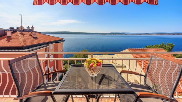A balcony with a table and chairs, a bowl of fruit, and a view of the sea. - Apartment Davor (Dramalj)