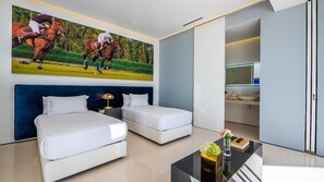 A modern hotel room with a large bed, a smaller bed, a desk with a lamp, and a painting of polo players on the wall.