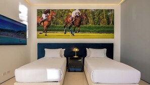 Habitación de hotel con dos camas, una mesita de noche con lámpara y un cuadro grande de jugadores de polo en la pared.